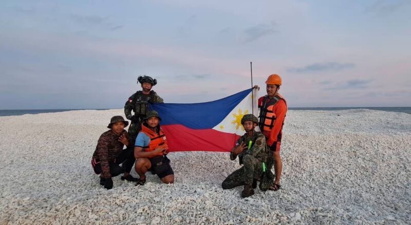 Philippines Coast Guard’s personnel unfurling a flag on a disputed isle in the South China Sea on April 27, 2025.